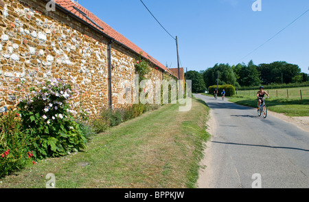 Radfahrer, vorbei an einer traditionellen Backstein und Feuerstein errichtet Gebäude während ganz Feldweg von North Norfolk auf Tournee Stockfoto