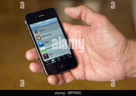 Das iPhone 4 in der Handfläche der Hand eines Mannes. Auf dem Bildschirm sehen Sie den App Store. Stockfoto