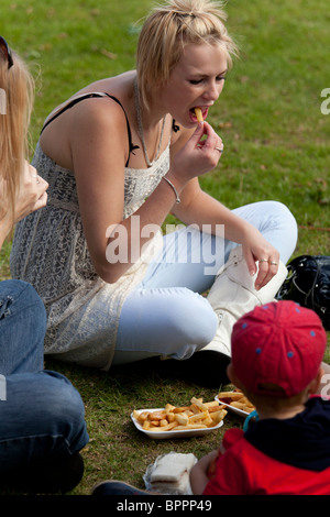 Mädchen saß auf dem Rasen essen Chips auf einer Land-Messe Stockfoto