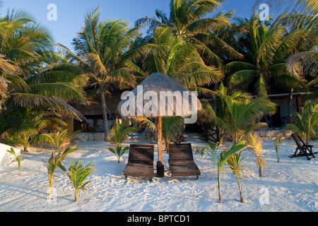 Palapa, flankiert von 2 hölzerne Liegestühle am Strand der Isla Holbox, Bundesstaat Quintana Roo, Mexiko. Stockfoto