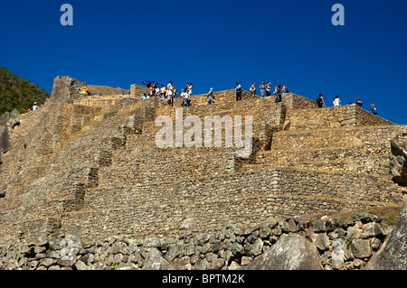 Touristen inmitten der komplizierten Steinarbeiten von zerstörten Gebäuden und Gartenterrassen an der alten Inka-Stadt Machu Picchu, Peru. Stockfoto