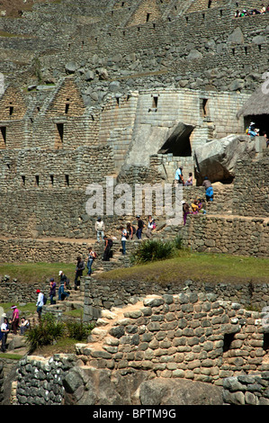 Touristen inmitten der komplizierten Steinarbeiten von zerstörten Gebäuden und Gartenterrassen an der alten Inka-Stadt Machu Picchu, Peru. Stockfoto