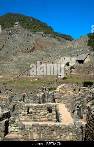 Touristen inmitten der komplizierten Steinarbeiten von zerstörten Gebäuden und Gartenterrassen an der alten Inka-Stadt Machu Picchu, Peru. Stockfoto