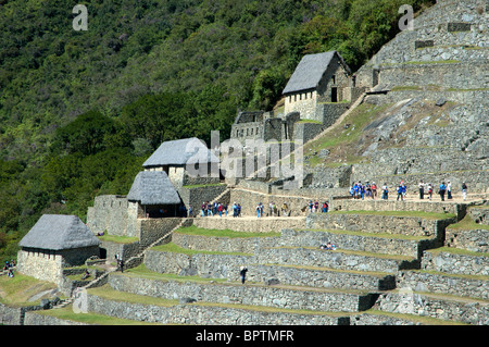 Touristen inmitten der komplizierten Steinarbeiten von zerstörten Gebäuden und Gartenterrassen an der alten Inka-Stadt Machu Picchu, Peru. Stockfoto