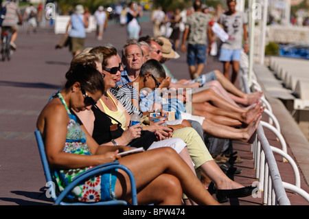 Menschen sitzen auf Bänken an der Promenade des Anglais, Nizza Stockfoto