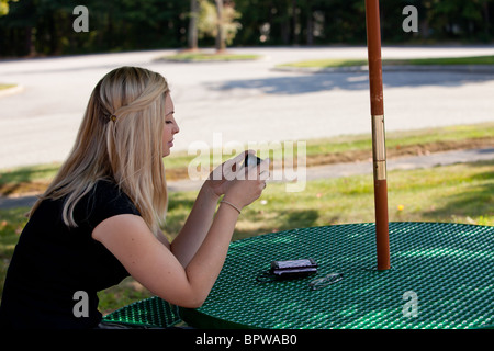 Junge, blonde Frau SMS auf ihrem Smartphone draußen an einem Tisch zu sitzen. Stockfoto