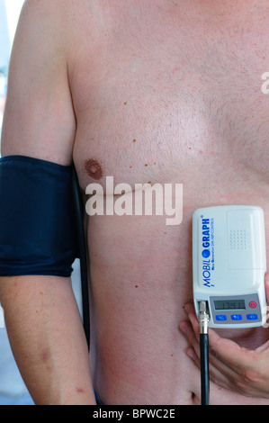 Mann mittleren Alters eine Blutdruckmanschette Arm trägt, und hält eine Mobil-O-Graph, Ambulatory Blood Pressure Monitor Stockfoto