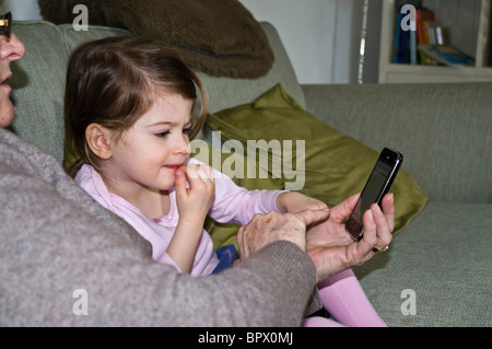 dh GIRL UK Oma und Enkelkind rätseln über iPhone Computerspiel lernen Kleinkind Kind kleine Kinder Kinder spielen Blick auf Telefon zu Hause Stockfoto