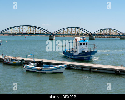 Ruderboot und Fischerboot im Hafen von Portimeo, Portimeo, Algarve, Portugal mit triple Bridge im Hintergrund Stockfoto