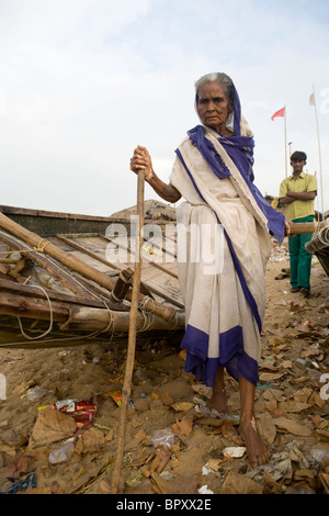 Blinde alte indische Frau spaziert am schmutzigen Strand zwischen zwei Fischerboot bei der Fischer-Villaga in Puri, Orissa, Indien Stockfoto