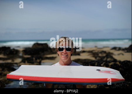 ein junger Mann, Jugendlicher, an einem sonnigen Tag am Strand von Whipisderry, in der Nähe von Newquay, mit einem Bodyboard stehend Stockfoto