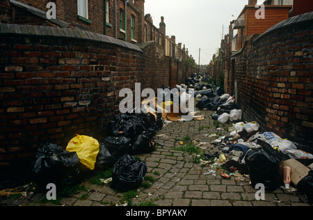 Armen Reihenhaus wohnen und Gasse in Liverpool, England, mit schwarzen Müll Taschen sind gegen industrielle Ziegelmauern links Stockfoto