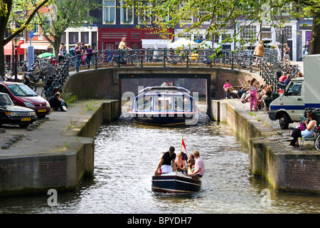 Amsterdam. Grachtenfahrt Ausflugsschiff und kleine Schaluppe im Leliegracht Kanal mit Straßencafés. Touristen sitzen und beobachten. Stockfoto