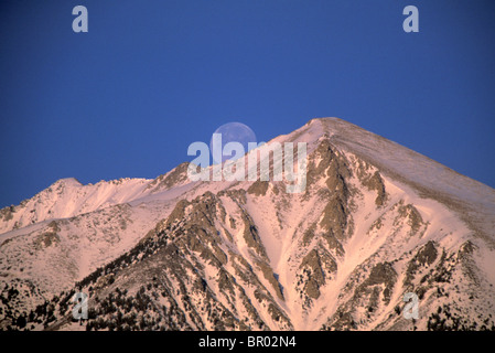 Einen malerischen Blick auf den Mond aufgehen über einem schönen Berggipfel wie Sonnenuntergang Alpenglühen es mit einem rosigen Glanz Farben. Stockfoto