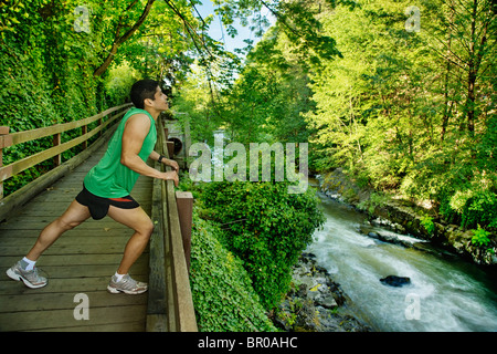 Gemischte Rassen Läufer stretching auf Gehweg nahe Fluss Stockfoto