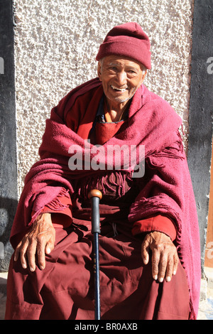 Älterer buddhistischer Mönch in roten Roben, mit Rohrstock, der eigentlich ein High-Tech-Wanderer Gehstock ist.  Die Besucher haben sehr gerne. Stockfoto