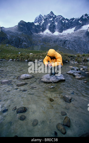 Ein Mann filtert das Wasser aus einem Gebirgsbach. Stockfoto