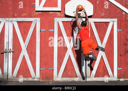 Schwarzer Mann dunking Basketball außerhalb Scheune Stockfoto