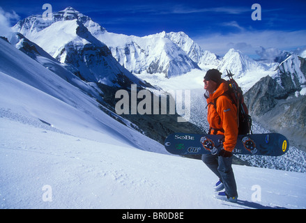 Ein Mann mit seinem Snowboard klettert eine Bergkette mit einem Gletscher im Hintergrund. Stockfoto