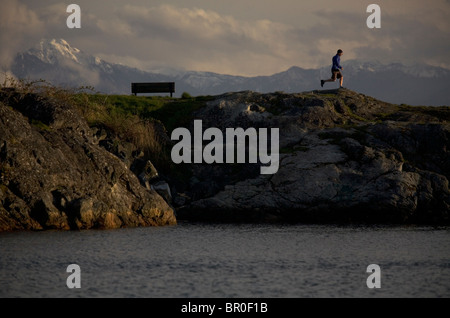 Mann, die entlang einem Wellenbrecher mit Wasser im Vordergrund und Berg Hintergrund. Stockfoto