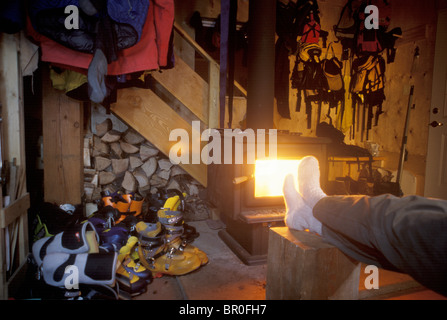 Ein Mann, Socken, wärmt die Füße durch einen Holzofen in einer Lodge in BC, Kanada. Stockfoto