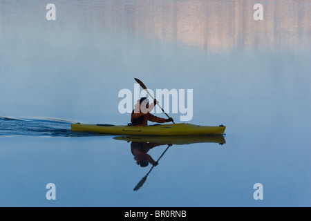 Ein Mann Kajak im Morgengrauen durch Berg Reflexionen auf Donner Lake, Kalifornien. Stockfoto