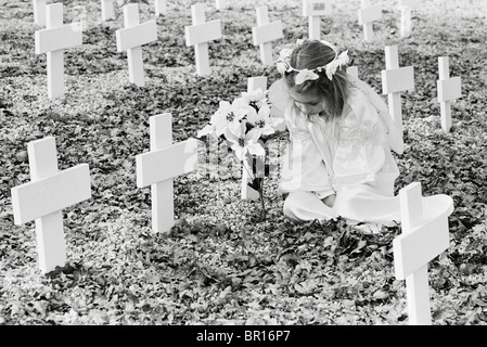 Ein junges Mädchen mit Blumen auf einem Friedhof. Stockfoto