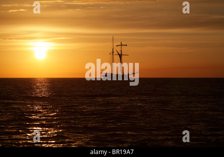 Ein Großsegler vor Anker in einer Bucht, die Silhouette gegen den Sonnenaufgang am Morgen. Stockfoto