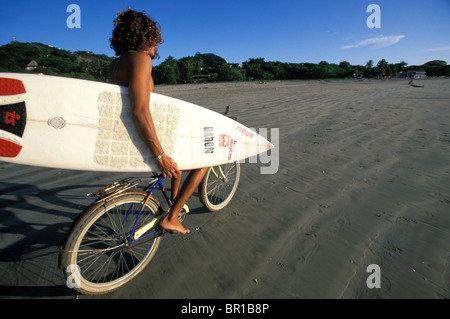 Mann sein Fahrrad am Strand entlang und das Festhalten an seinem Surfbrett in Tamarindo, Costa Rica. Stockfoto