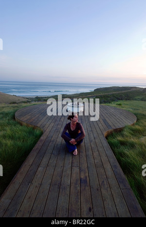 Eine Frau Yong beobachtet den Sonnenuntergang von einem Deck mit Blick auf den Pazifischen Ozean in Hollister Ranch, California. Stockfoto