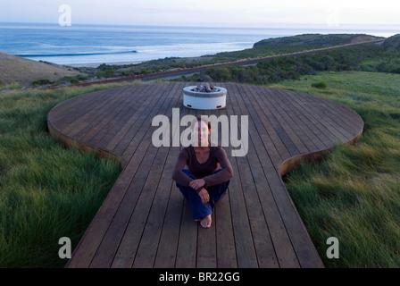 Eine Frau Yong beobachtet den Sonnenuntergang von einem Deck mit Blick auf den Pazifischen Ozean in Hollister Ranch, California. Stockfoto