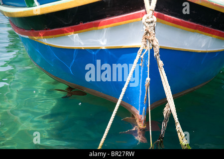 Traditionelle maltesische Luzzu Holzboot bemalten Bogen und Seilen vor Anker in klarem Wasser in Malta Stockfoto