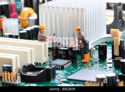 Technischer Support - Makroaufnahme einer Computer-Hauptplatine und zwei kleinen Spielzeug-Ingenieure Befestigung etwas, Konzept. Stockfoto