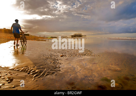 Radfahrer mit Fahrrad auf Hove Beach.  Blick Richtung Brighton und die verlassenen Pier West bei Ebbe, East Sussex, England Stockfoto