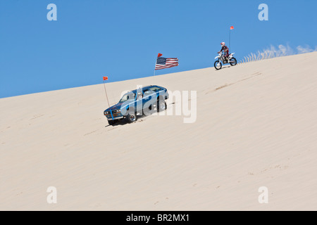 Ein Teenager, der mit dem Motorrad durch Sanddünen fährt, und ein Auto mit US-Flagge in Michigan, MI, USA, aus einem niedrigen Winkel außerhalb des Horizonts des US-Lifestyle-Lebens in Hochauflage Stockfoto