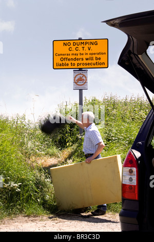 Ein Mann wirft einem Beutel mit Müll in einen Feldweg unter einem "kein dumping" Zeichen welche Zustände, die CCTV-Kameras in Betrieb sind Stockfoto