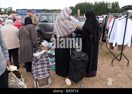 Kleidung für den Verkauf auf Tabelle am Flohmarkt in Surrey, England, von muslimischen Burka untersucht bekleideten Frauen Stockfoto