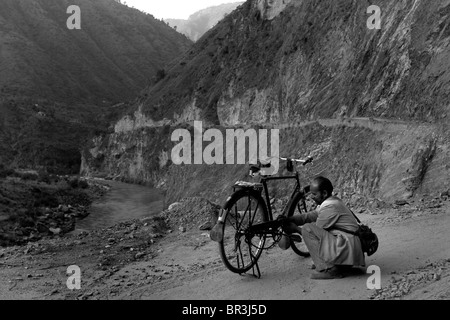 Ein Mann repariert eine flache Reifenschaden auf seinem Fahrrad auf einer abgelegenen Bergstraße im Himalaya in Himachal Pradesh in Indien. Stockfoto