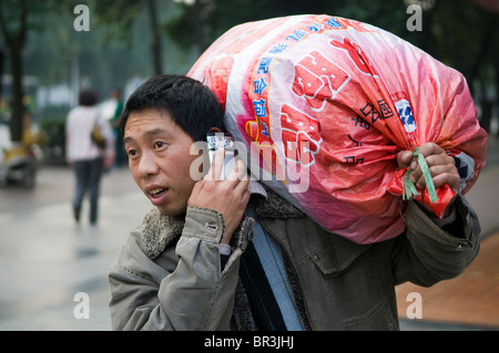 Arbeiter trägt schweren Sack während des Gesprächs auf Mobiltelefon, Chengdu, Sichuan Provine, China Stockfoto