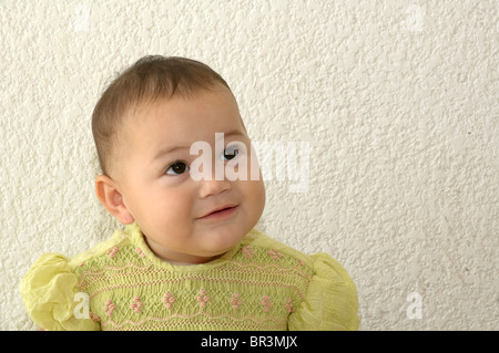 Tulum, Quintana Roo/Mexiko - Mai 4: Babymädchen im grünen Kleid wegsehen von Kamera Sitzgelegenheiten gegen weiße Wand Stockfoto