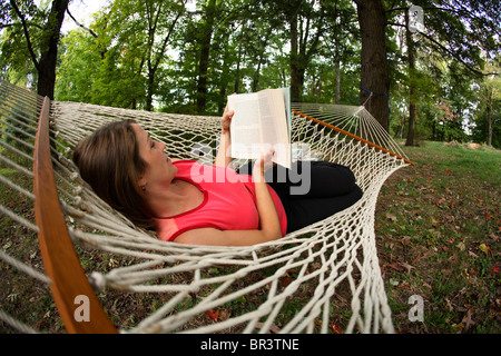 Junge Frau, die ein gutes Buch in der Hängematte in ihrem Hinterhof in Fayetteville, WV Stockfoto