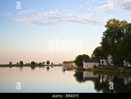 Spiegelglatten Wasser spiegelt Bäume und Gebäude entlang einen Hafen an einem ruhigen Sommermorgen Stockfoto