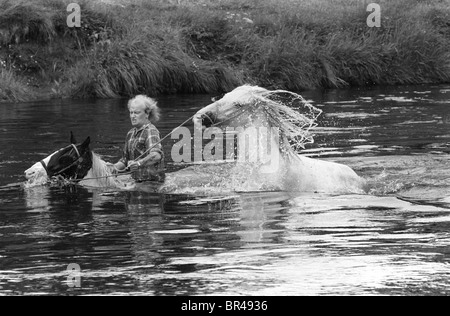 Zigeuner reitet auf seinem Pferd und führt einen anderen in den Fluss Eden, um sich gut zu waschen. Horse Fair River Eden wäscht sie vor dem Verkauf. Appleby in Westmorland Cumbria .1981 1980s UK HOMER SYKES Stockfoto