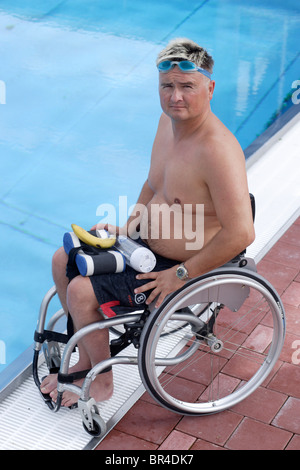 Jungen, behinderten Mann im Rollstuhl am Rande eines Swimmingpools schwimmen Übungen, schaut in die Kamera Stockfoto