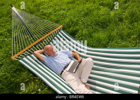 Älterer Herr liegen in der Hängematte mit einem netbook Stockfoto