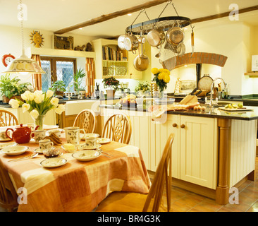 Frühstück am Tisch mit aufgegebenen Tuch im Essbereich der große Landhausküche mit Pfannen auf Gestell oberhalb Insel Stockfoto