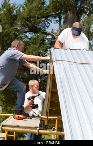 Bauarbeiter arbeiten auf Gerüsten anfügen Blech an den Sparren auf dem Dach einer Scheune mit Power Schraube Gewehren steht ein Stockfoto
