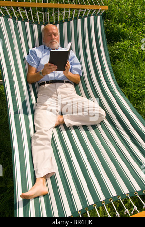 Älterer Herr liegen in der Hängematte, ein Buch zu lesen Stockfoto