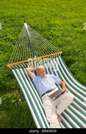 Älterer Herr liegen in der Hängematte mit einem netbook Stockfoto