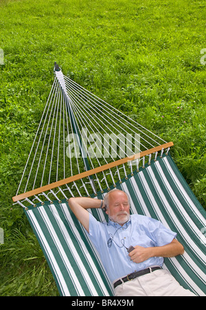 Älterer Herr liegen in der Hängematte und Musik hören Stockfoto